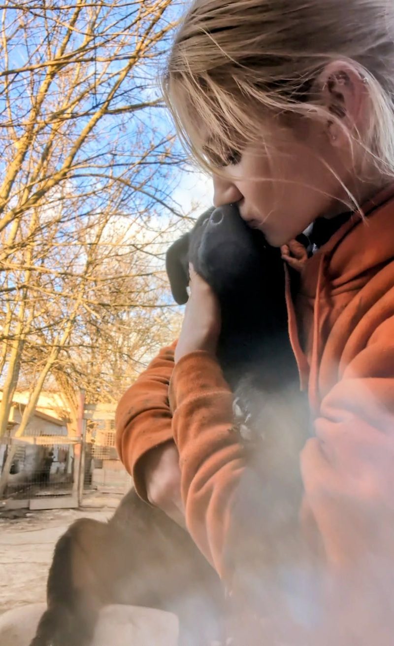 A caretaker gently holding and kissing a black puppy's head