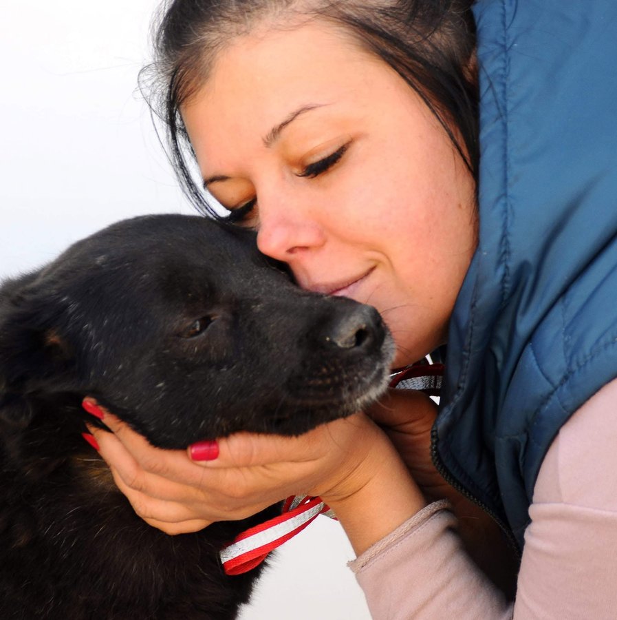 Founder Maryna Bolokhovets resting her forehead against a rescued black dog she is holding